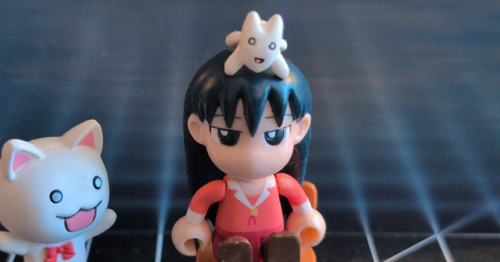 A Sakaki toy from Azumanga Daioh sitting on a chair with a cat on her head, and a cat-like creature standing next to her